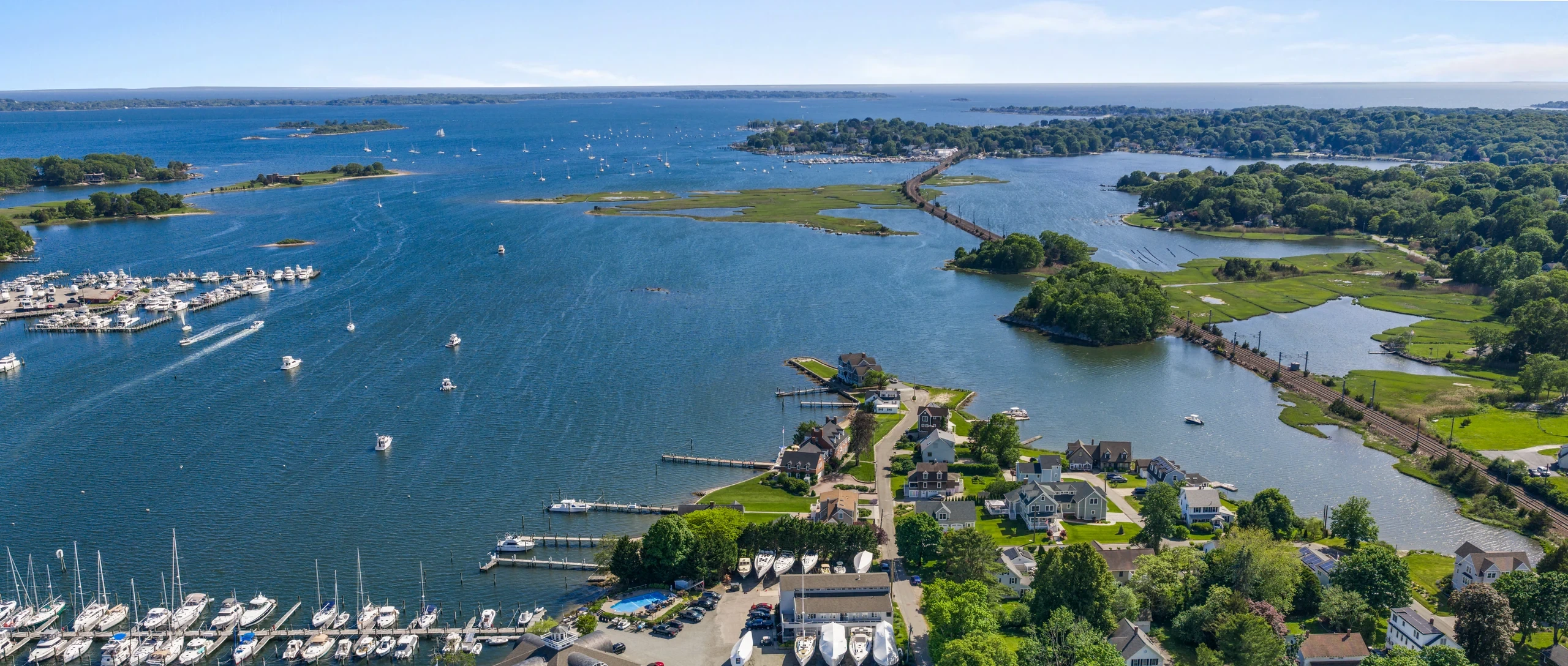 Wide aerial view across Mystic harbor, Willow Point, marinas, and open water.