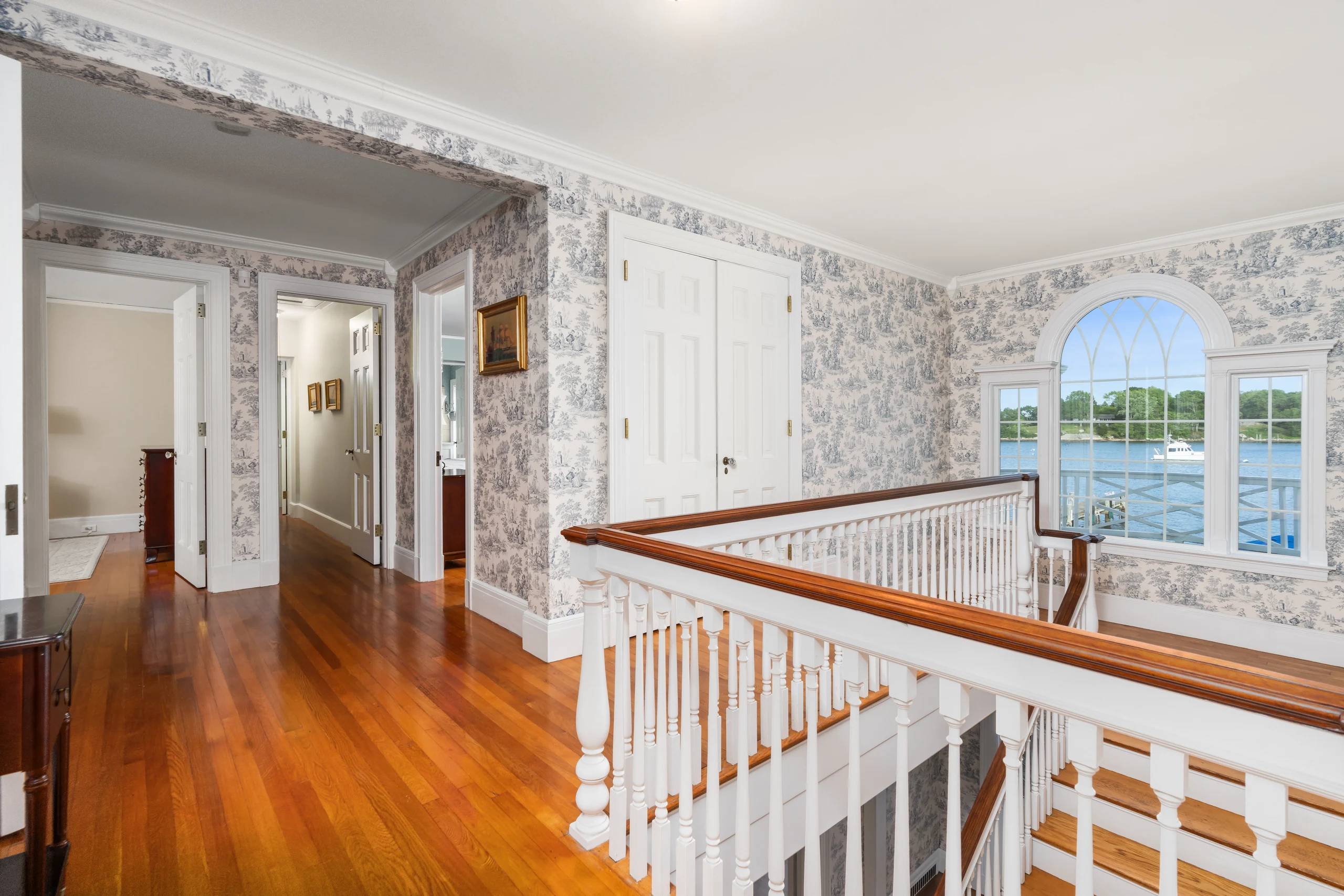 Upstairs landing with a turned-baluster railing and an arched window framing the water.