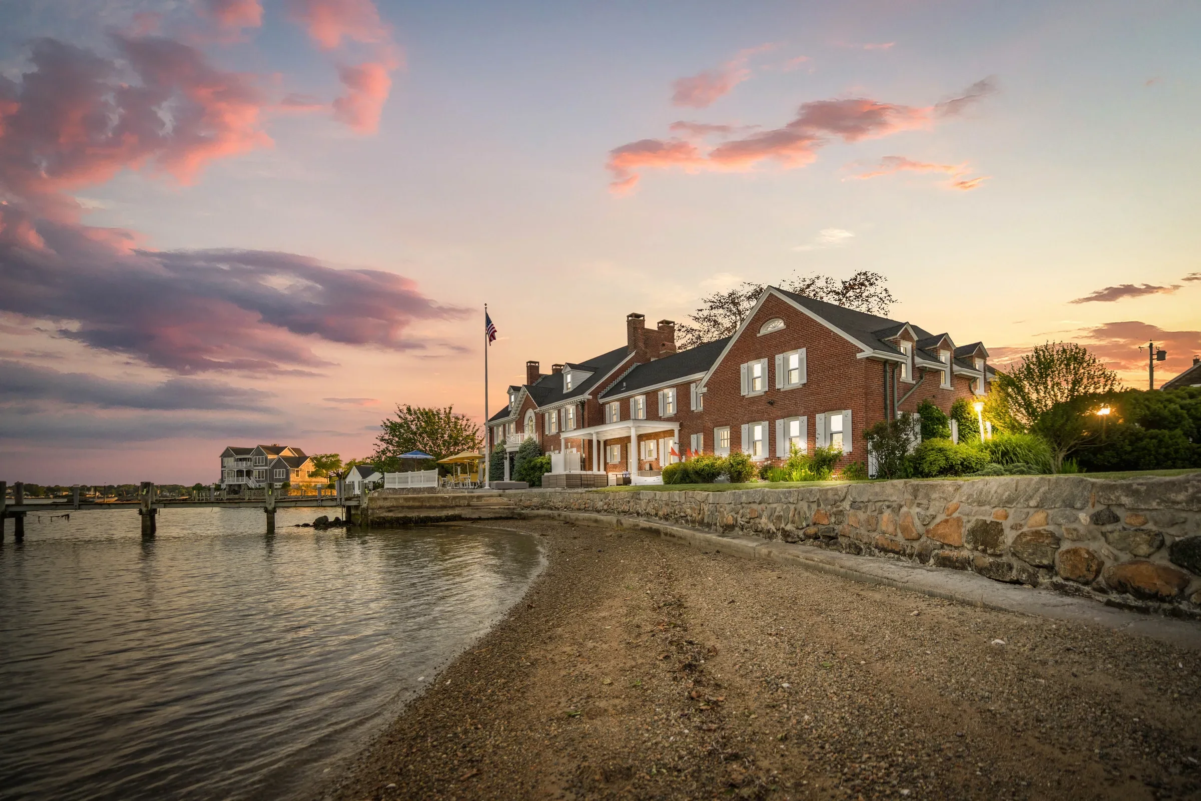 The brick Georgian Colonial seen from the beach below the stone seawall at twilight.