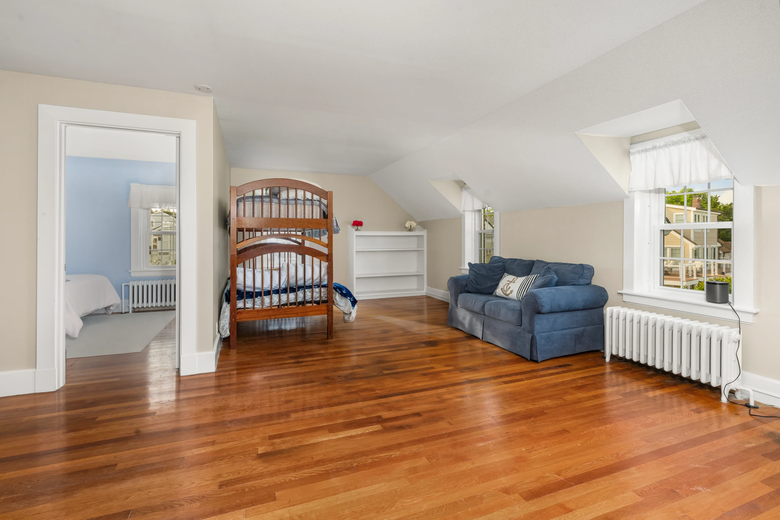 Upper-level sitting room with sloped ceiling, hardwood floors, sofa, and built-ins.